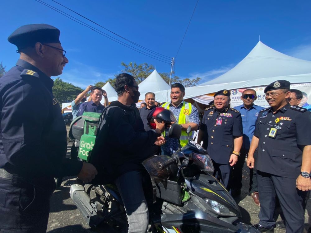  Shahelmey mengedarkan topi keledar kepada penunggang motosikal semasa pelancaran Kempen Kesedaran Keselamatan Jalan Raya di Teluk Dumpil Putatan.