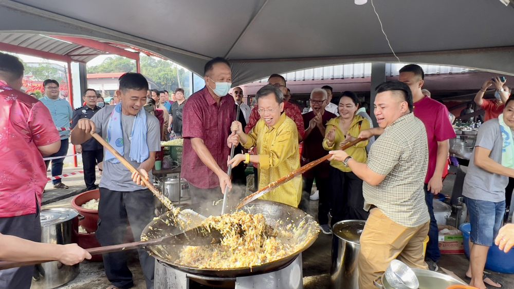 Dr Sim (dua kanan) dan Miro (kanan) bersama-sama menggaul makanan yang dimasak secara gotong-royong untuk pengunjung di pekan Siniawan sempena Chap Goh Mei. - Gambar Roystein Emmor