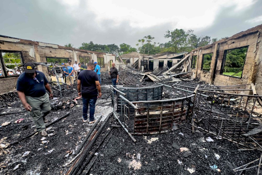  Sekumpulan pegawai penyiasat dan kakitangan kerajaan memeriksa asrama sekolah yang hangus dalam kebakaran di Guyana pada Ahad lepas.  — Gambar AFP