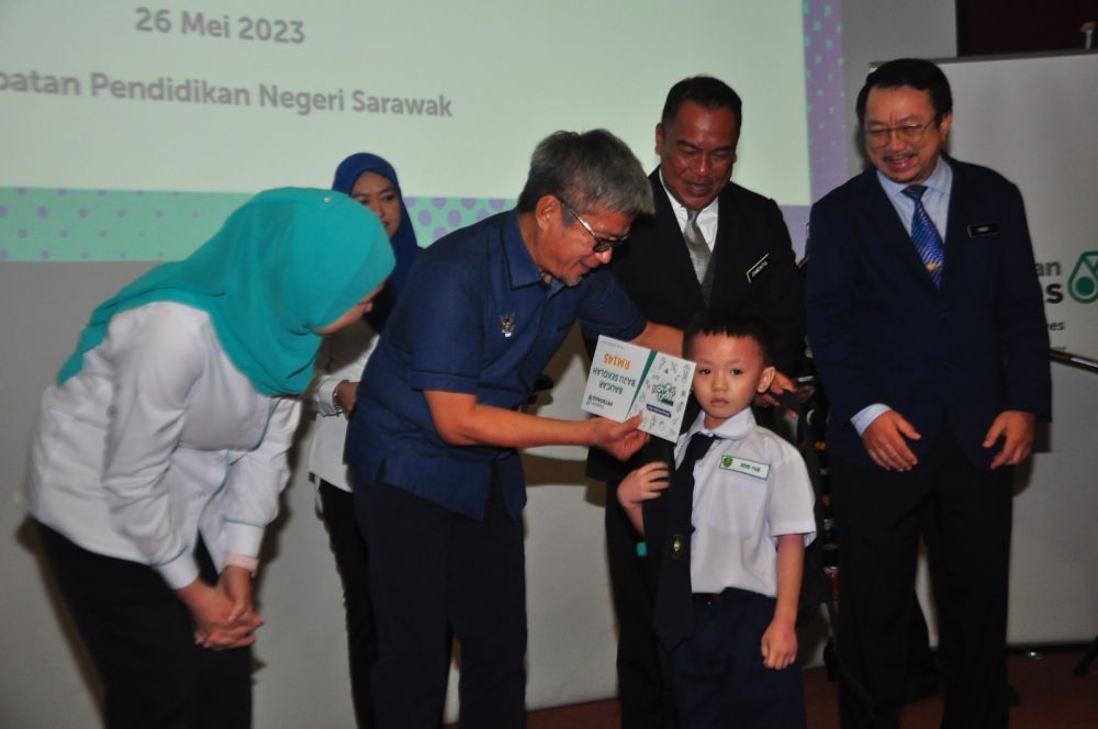 Dr Annuar menyampaikan kit bilik darjah kepada murid yang menerima peralatan sekolah daripada Yayasan Petronas pada majlis tersebut.