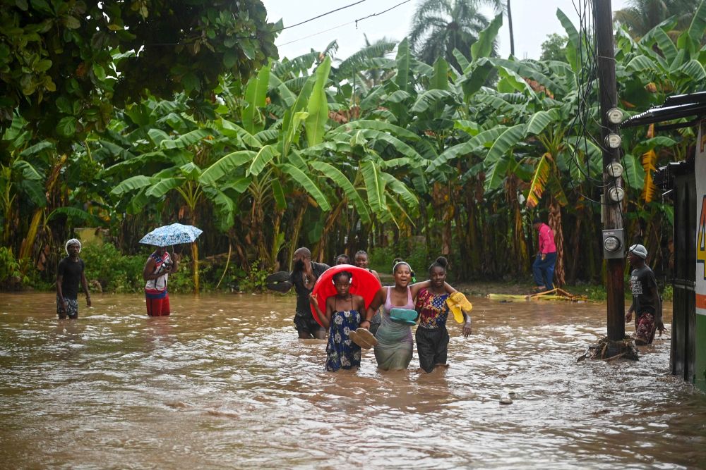  Penduduk mengharungi banjir di kawasan kejiranan Petit Goave semasa hujan lebat melanda Haiti, Sabtu lepas. — Gambar AFP