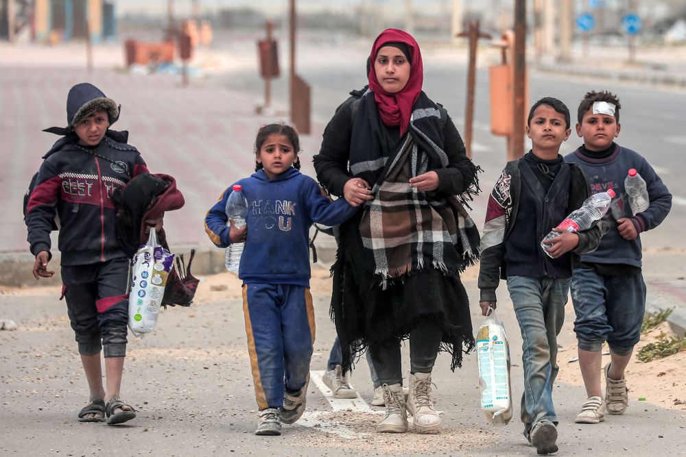 Seorang wanita berjalan kaki bersama anak-anaknya selepas melarikan diri daripada pengeboman di kawasan hospital Al-Shifa ketika mereka tiba di kem pelarian Nuseirat di tengah Semenanjung Gaza kelmarin. — Gambar AFP