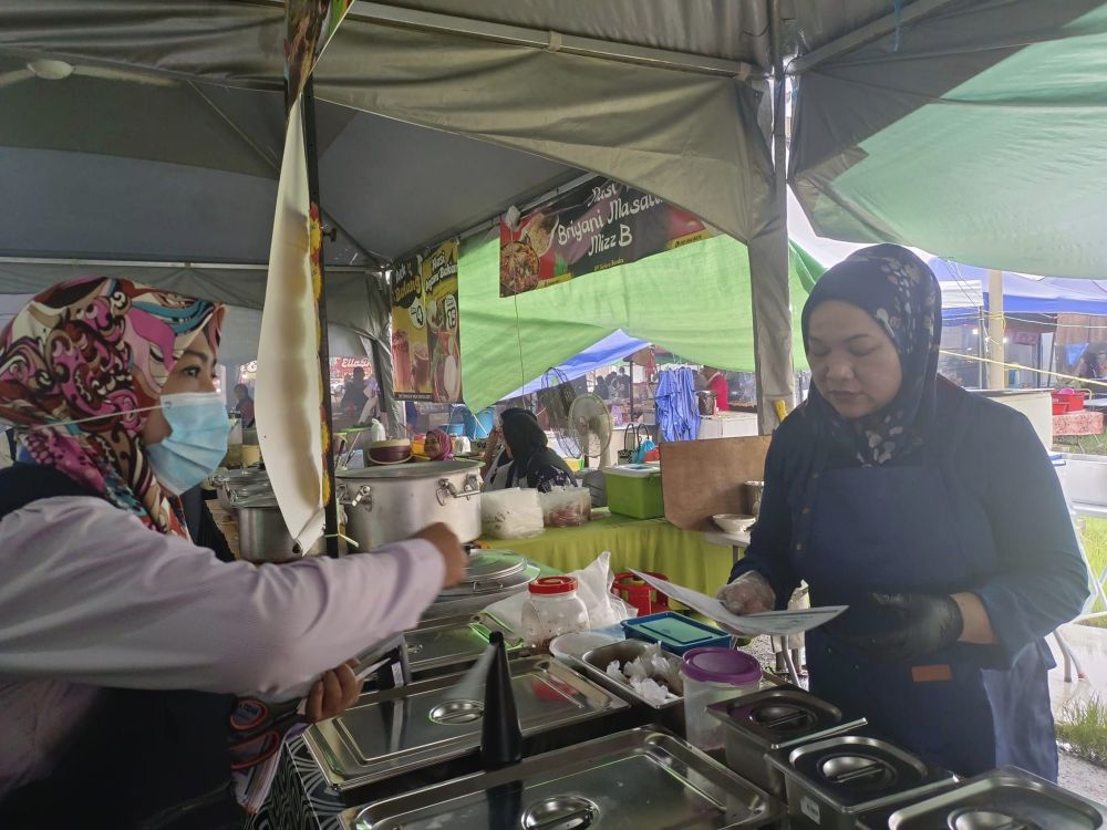Zaifa (kiri) mengedarkan risalah berkenaan penerapan aspek kebersihan dan keselamatan makanan semasa program di Bazar Ramadan Sri Aman pada Rabu.