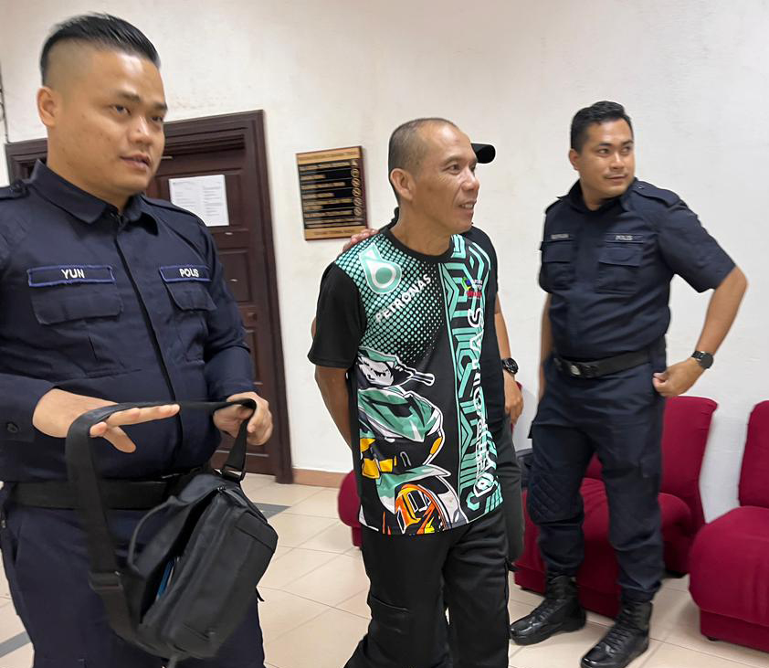 Polis mengiringi Madeng selepas prosiding di Mahkamah Sesyen, Kuching hari ini.