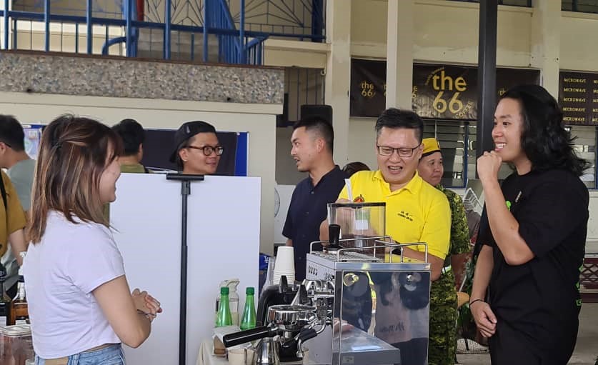 Chieng melawat salah satu gerai menjual minuman kopi sambil disaksikan Chris (kanan) pada Program Microwave di SMK Methodist, hari ini.
