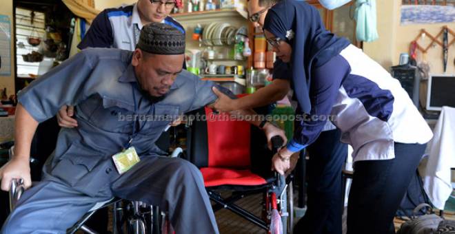 BANTU: Norashikin (kanan) bersama kakitangannya membantu Idris duduk di kerusi roda                     baharunya sumbangan Yayasan Bank Rakyat di kediamannya di Bota semalam. — Gambar Bernama