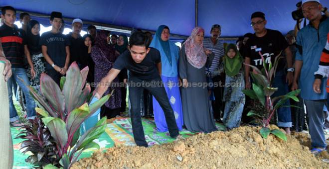 DISEMADI: Anak Allahyarham Ramli Abdul Majid, Muhammad Fauzi Ramli, 17, menyiram air di pusara bapanya pada majlis pengkebumian di Tanah Perkuburan Batu 14 di Puchong dekat Kuala Lumpur, semalam. — Gambar Bernama