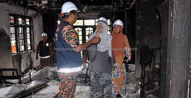 TINJAU: Anggota Jabatan Bomba dan Penyelamat bersama Tengku Mastura (tengah) meninjau keadaan rumahnya yang terbakar di Kampung Kuala Ibai di Kuala Terengganu semalam. — Gambar Bernama