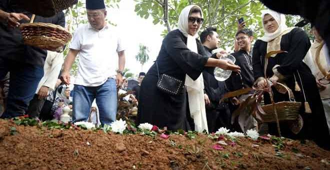 SELAMAT DISEMADI: Ida Neliaty Lokman (dua kiri) dan Danny Lokman (kiri) menyiram air bunga mawar selepas jenazah abangnya, Mahadzir selamat dikebumikan di Tanah Perkuburan Islam Bukit Kiara dekat Kuala Lumpur, semalam. — Gambar Bernama