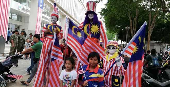 SEMANGAT MERDERKA: Adila (kanan) bersama bapa saudaranya, Rosli Y (tengah) dan Mohd Irwan yang memakai pakaian bertemakan Jalur Gemilang, menjadi tumpuan orang ramai ketika menyaksikan acara perarakan dan perbarisan sempena sambutan Hari Kebangsaan Ke-61 di Dataran Putrajaya, semalam. — Gambar Bernama