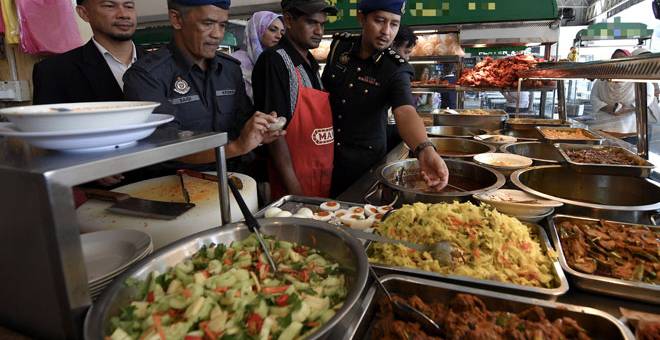 BERJAYA DIKESAN: Zulfahmy (kanan) bersama agensi penguatkuasaan lain memeriksa makanan yang dijual di sebuah restoran, semalam. Kedai makanan tersebut dikesan meletakkan logo halal di bahagian belakang kedai dan tidak pernah memohon sijil halal.  — Gambar Bernama