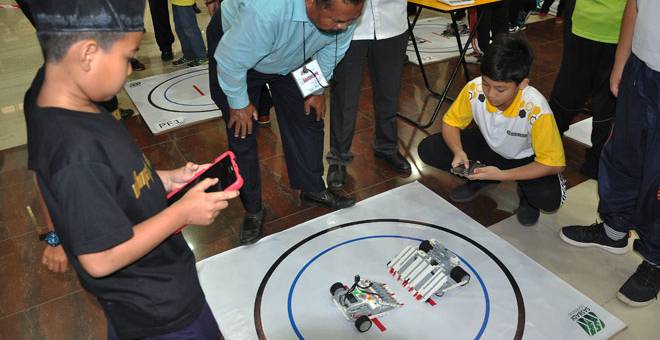 BUKAN PENGHALANG: Dua peserta terdiri dari pelajar sekolah menggunakan kemahiran dan kecekapan mereka mengendalikan robot masing-masing pada pertandingan ‘Mizanis Robotic Sumo Battle 2019’ anjuran Institut Pendidikan Guru Kampus Sultan Mizan (IPGKSM) di Besut, semalam. — Gambar Bernama