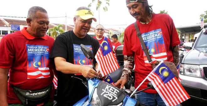 SEMANGAT PATRIOTIK: Amiruddin (tengah) memasang bendera Jalur Gemilang pada motosikal seorang peserta sempena Program Konvoi Jelajah Merdeka Parlimen Kubang Pasu di Dataran Darulaman di Jitra, semalam. — Gambar Benama