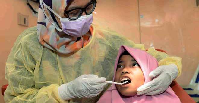 PEMERIKSAAN: Dr Nur Syaira memeriksa keadaan gigi Adrina Afifah di klinik pergigian bergerak pada Program Dash for Smile anjuran Bahagian Kesihatan Pergigian Kedah di Pantai Murni Waterfront, Yan semalam. — Gambar Benama