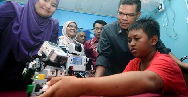 BERBAKAT: Saifuddin melihat adik Ahmad Syahril semasa melihat teknologi robot yang dipamerkan pada Majlis Pelancaran Rumah Ilmu Telok Air Tawar semalam. — Gambar Benama