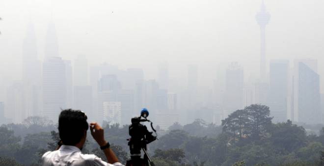 Seorang jurukamera dilihat merakam video keadaan ruang udara Kuala Lumpur yang diselubungi jerebu tebal dengan bacaan IPU 160 iaitu pada tahap tidak sihat ketika dirakam pada 1 tengah hari, hari ini. - Gambar Bernama 