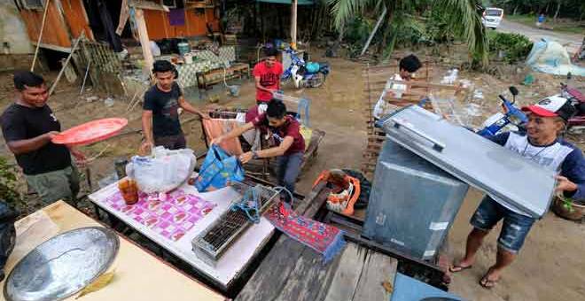 GOTONG-ROYONG: Raja Firdaus Raja Kamaruddin, 24, (kiri) dibantu rakan-rakannya mengemas kedai makanan milik keluarganya yang rosak selepas dilanda banjir ketika tinjauan di Kampung La, Jerteh semalam. — Gambar Bernama