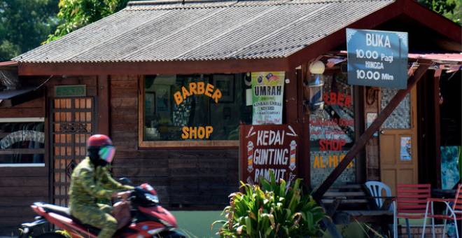 Seorang anggota Rela menunggang motosikal melintasi sebuah kedai gunting rambut di Kampung Peramu, Kuantan baru-baru ini. - Gambar Bernama 