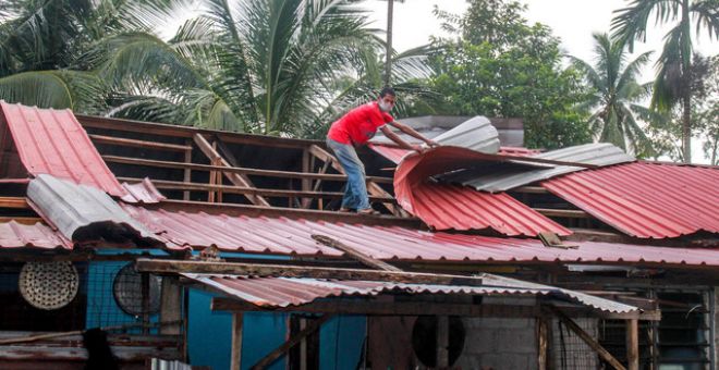 Penduduk kampung membaiki atap yang diterbangkan ribut dalam kejadian berlaku lewat petang semalam di Kampung Nara, hari ini. -Gambar Bernama.