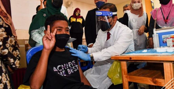 Dr Noor Azmi melakukan proses suntikan vaksin kepada Muhammad Iqbal Ishak, 11, di Dewan Seri Selinsing, Gunung Semanggol di Bagan Serai hari ini. -Gambar 