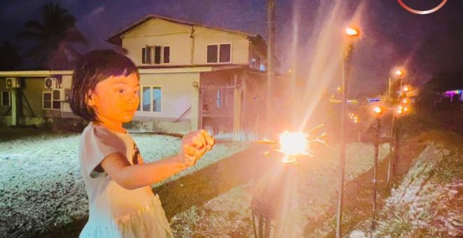 Alfrina yang berusia enam tahun menyalakan bunga api menggunakan pelita yang dipasang di hadapan rumah keluarganya di Kampung Segedup, Kuching. Umat Islam di seluruh dunia menyambut Hari Raya Aidilfitri hari ini, menandakan berakhirnya bulan suci Ramadan. - Gambar Roystein Emmor
