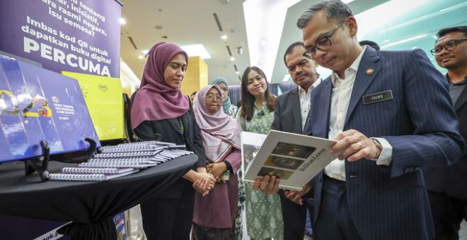 Fahmi (kanan) meneliti buku Bidikan Lensa selepas merasmikan program Jom Baca Bersama 10 Minit bertemakan "Pembacaan Melestarikan Perpaduan" Peringkat Kementerian Komunikasi hari ini. Turut sama Timbalan Menteri Teo Nie Ching (tiga, kiri) dan Ketua Setiausaha Kementerian Komunikasi, Datuk Mohamad Fauzi Md Isa (empat, kiri).-Gambar BERNAMA