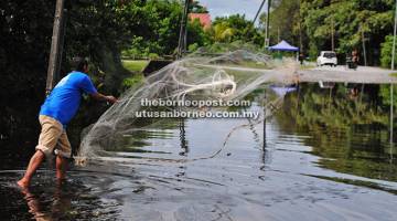 LUBUK REZEKI: Effandi menebar jala di sebatang jalan raya ditenggelami air bertakung berhampiran rumahnya akibat akibat hujan lebat.