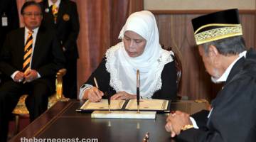 ANGKAT SUMPAH: Jamilah menandatangani dokumen di hadapan Asfia (kanan) sambil disaksikan Abang Johari (belakang) selepas mengangkat sumpah sebagai ADUN Tanjong Datu di Kuching, semalam.