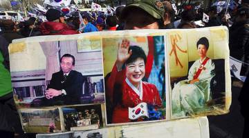 TETAP DISANJUNG: Seorang penyokong menunjukkan kolaj gambar Park (tengah), bapa dan ibunya di luar pejabat pendakwa raya di Seoul, semalam. — Gambar AFP