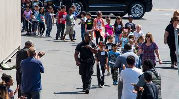 BERI SEMANGAT: Seorang pegawai polis mengetuai barisan pelajar sekolah yang akan diserahkan kepada ibu bapa masing-masing sejurus selepas kejadian berdarah di San Bernardino, California kelmarin. — Gambar AFP
