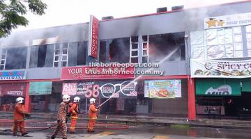 PADAM: Anggota bomba berusaha memadam kebakaran tiga unit tingkat atas bangunan kedai tersebut.