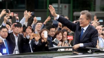 TERAJU BAHARU: Moon melambaikan tangannya ke arah orang ramai yang berbaris di sepanjang jalan raya dalam perjalanan ke Rumah Biru selepas upacara angkat sumpah jawatan di Seoul, semalam. — Gambar Reuters