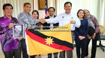 SERAH: Pahon menyerahkan bendera Sarawak kepada Bojeng sambil disaksi Ipoi (kiri) dan tetamu kehormat lain.