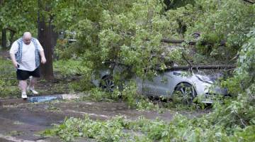 REMUK: Seorang lelaki melintasi sebuah kereta yang ditimpa pokok tumbang akibat ribut kuat di Moscow, kelmarin. — Gambar Reuters