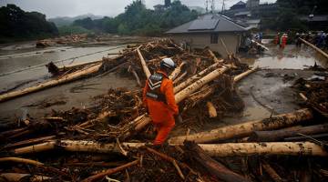 PENCARIAN SUKAR: Seorang anggota penyelamat berjalan di atas serpihan kayu yang dihanyutkan hujan lebat ketika operasi mencari orang hilang berhampiran sebuah rumah yang rosak akibat banjir besar di daerah Yamada di Asakura, wilayah Fukuoka, Jepun semalam. — Gambar Reuters