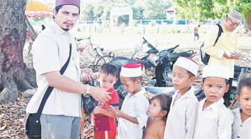 SUMBANGAN: Ustaz Ahmad Abdul Hamid memberi wang kepada para pelajar sekolah agama Kampung Prik Bui.