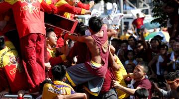 PERHIMPUNAN KEAGAMAAN: Para penganut berpaut pada salib yang membawa imej Black Nazarene semasa perarakan tahunan Roman Katolik di Manila, semalam. — Gambar Reuters