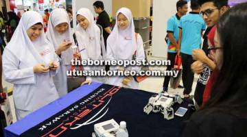 MINAT: Pelajar sekolah singgah di gerai pameran untuk mencuba permainan robotik. 