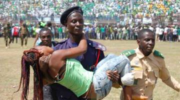 DIBANTU: Seorang wanita yang cedera dalam rempuhan itu dibawa anggota polis ke tempat selamat semasa majlis angkat sumpah Bio di Freetown, kelmarin. — Gambar AFP