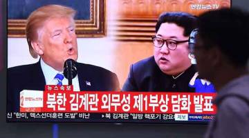 UGUT BATAL: Seorang lelaki berjalan melintasi skrin berita televisyen menunjukkan Kim (kanan) dan Trump di stesen kereta api di Seoul semalam. — Gambar AFP