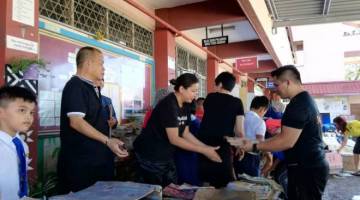  JENIFER (dua kiri) turut sama menyusun buku sekolah yang rosak akibat banjir.