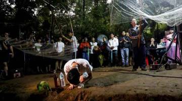 DOA SELAMAT: Ahli keluarga dan saudara-mara melakukan upacara agama di hadapan pintu masuk utama ke gua Tham Luang selepas 12 kanak-kanak hilang bersama jurulatih mereka di gua tersebut di Chiang Rai, Thailand semalam. — Gambar AFP 