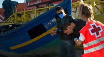 DIBANTU: Seorang pendatang dipapah anggota Guardia Civil Sepanyol dan ahli Palang Merah sejurus tiba di pelabuhan Algeciras, kelmarin. — Gambar AFP