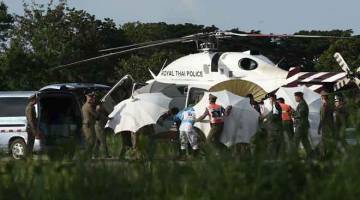 MISI BERJAYA: Anggota pasukan keselamatan menggunakan payung untuk menutup pemandangan di sekitar sebuah usungan berhampiran helikopter dan ambulans di lapangan terbang tentera di wilayah Chiang Rai, Thailand kelmarin. — Gambar AFP