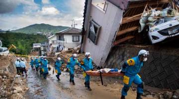 BERGOTONG-ROYONG: Anggota polis membantu dalam kerja membersihkan serpihan di jalan raya selepas banjir melanda kawasan kejiranan di Kumano, wilayah Hiroshima kelmarin. — Gambar AFP