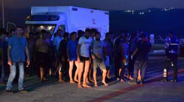 YANG SELAMAT: Pendatang berbaris di sebelah ambulans ketika mereka menunggu di pelabuhan Tasucu di Mersin kelmarin selepas bot mereka karam di Laut Mediterranean di luar bahagian utara Cyprus. — Gambar AFP