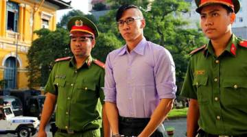 DIBICARAKAN: Nguyen (tengah) diiringi oleh dua anggota polis sebelum perbicaraannya di mahkamah di bandar Ho Chi Minh semalam. — Gambar Reuters