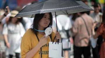 PANAS: Seorang wanita menggunakan kipas angin kecil untuk menyejukkan badannya di Tokyo semalam akibat gelombang haba ‘luar biasa’ melanda Jepun sejak awal bulan ini. — Gambar AFP