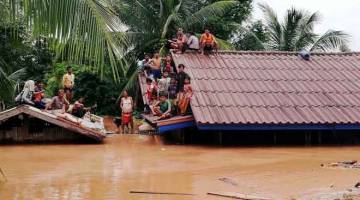 BANJIR KILAT: Penduduk berlindung di atas bumbung rumah mereka selepas empangan kuasa hidro Xe-Namnoy melimpah dan menyebabkan banjir kilat di wilayah Attapeu di selatan Laos kelmarin. — Gambar ABC Laos News/Reuters