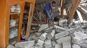 TRAGEDI: Gambar serahan Antara menunjukkan seorang penduduk kampung menggeledah puing sebuah rumah yang ranap semasa pencarian bagi barang-barang milik pelancong Malaysia yang maut semasa gempa bumi melanda kampung Sembalun Selong di Lombok Timur, semalam. — Gambar Reuters